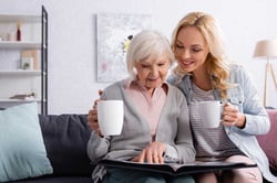 smiling-elderly-woman-cup-looking-photo-album-daughter-625x417